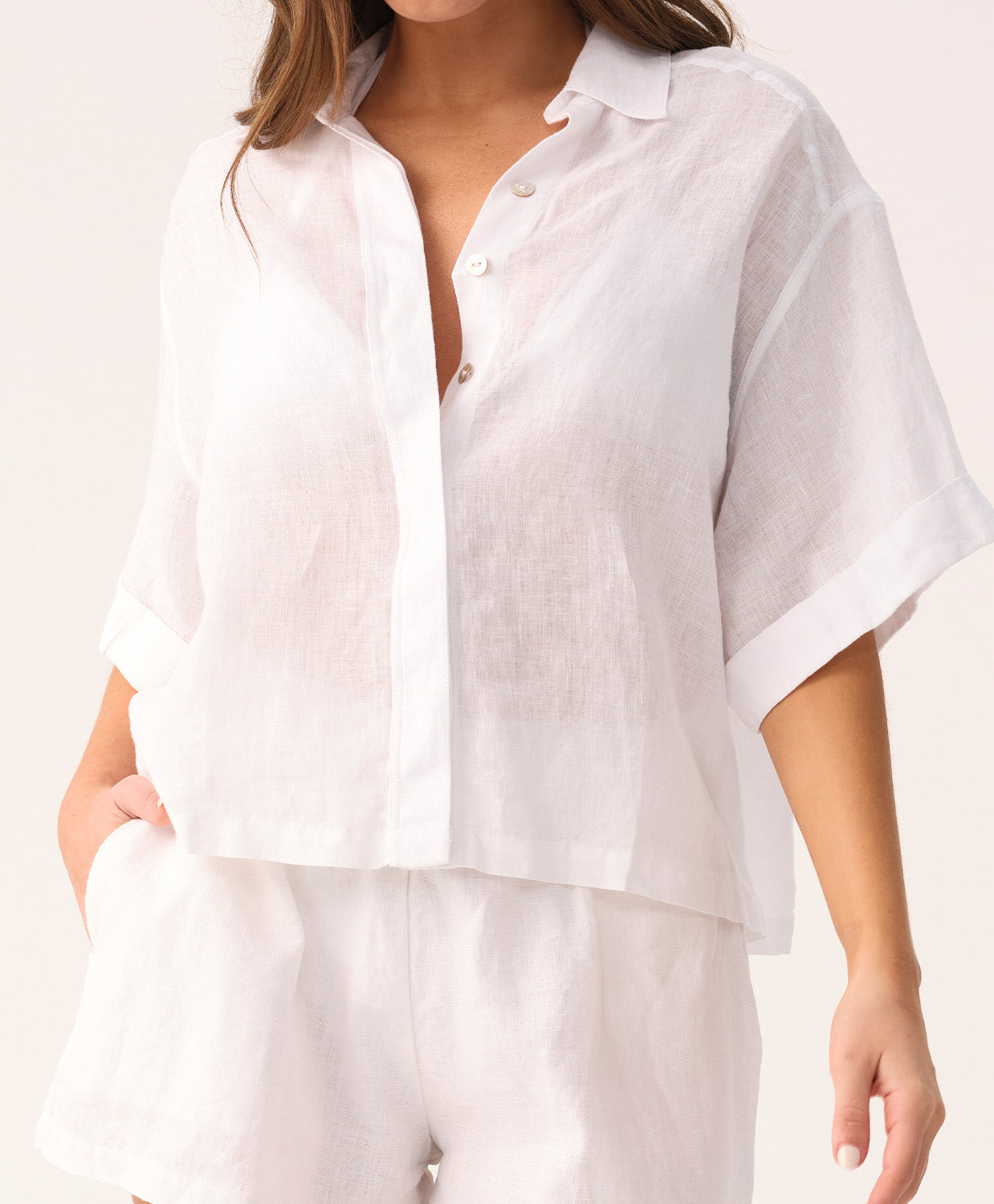 Woman wearing a white short sleeve shirt and short set on a plain background