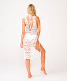 A woman wearing a white lace cover up dress facing a white wall.