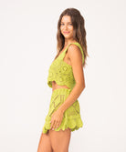 A woman wearing a matching green crochet tank and skirt set standing against a white wall.