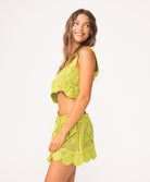 A woman wearing a matching green crochet tank and skirt set standing against a white wall.