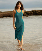 A woman wearing a teal mid length dress walking on the beach.