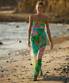 A woman wearing a long floral print dress walking on the beach near the ocean.