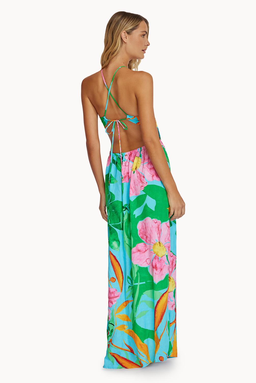 A woman wearing a long floral print dress facing towards a white wall.