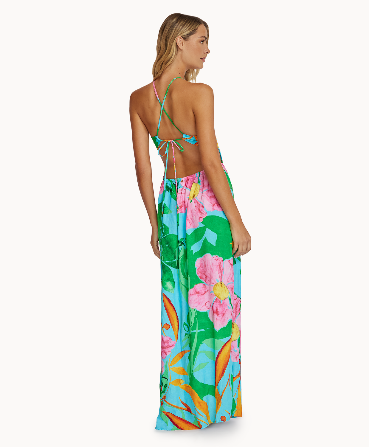 A woman wearing a long floral print dress facing towards a white wall.
