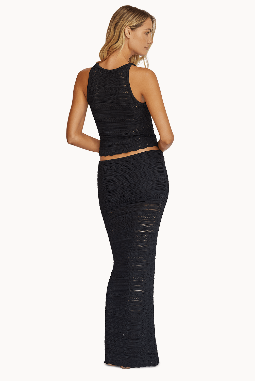 Back view of a woman wearing a matching black knit top and skirt in front of a white background.