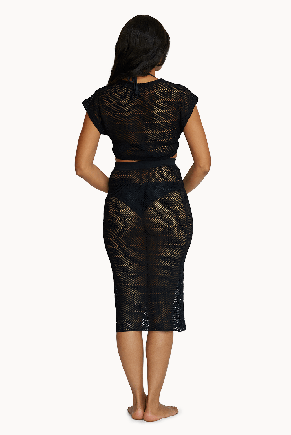 Back view of a woman wearing a matching black knit top and skirt in front of a white background.