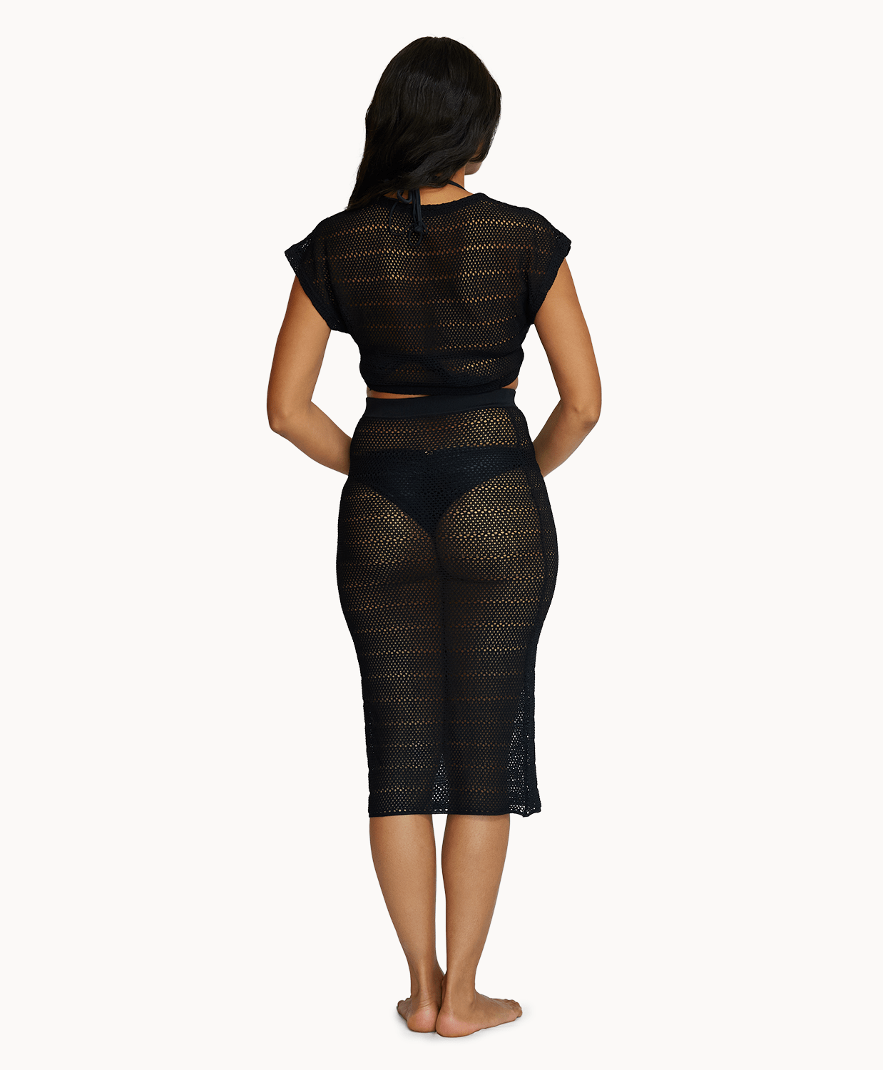 Back view of a woman wearing a matching black knit top and skirt in front of a white background.