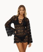 Woman wearing black lace tunic in front of a white background.