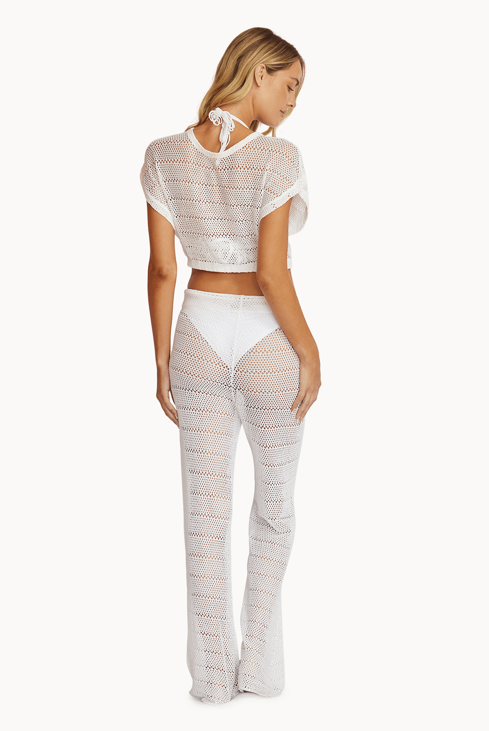 Back view of woman wearing matching white, crochet top and pants in front of a white background.