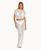 Woman wearing a matching cream knit top and pants in front of a white background.