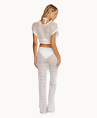 Back view of a woman wearing a matching cream knit top and pants in front of a white background.