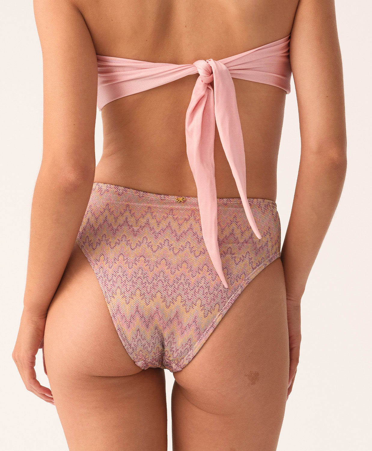 Woman wearing a pink bikini with a geometric pattern on a plain background