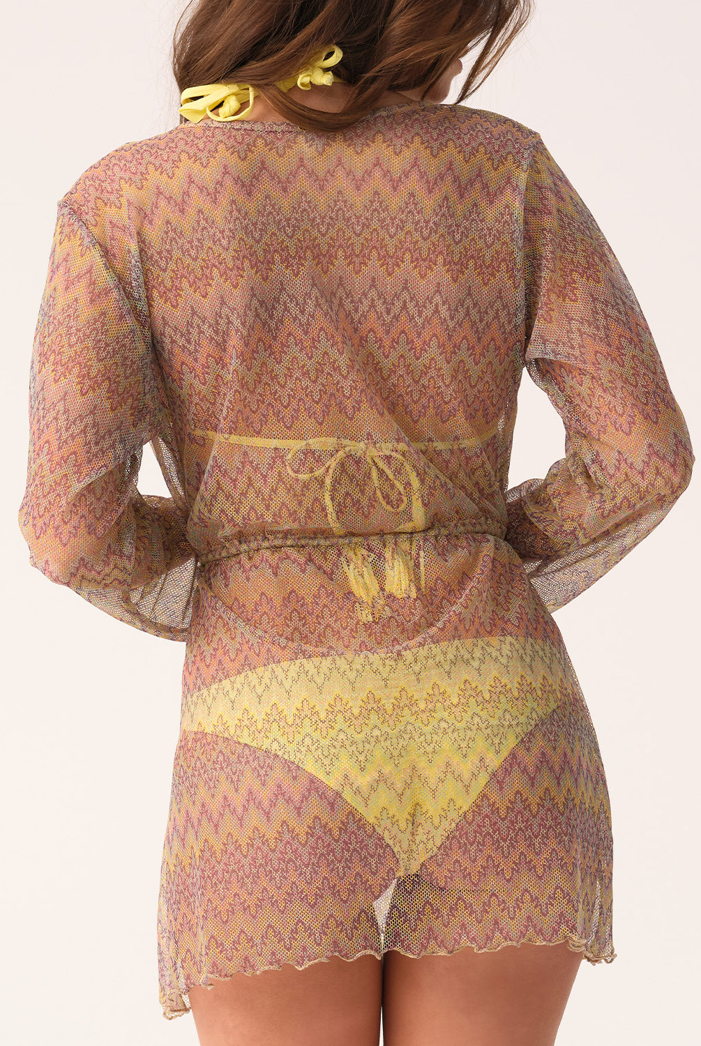 Woman wearing a patterned sheer outfit with a belt on a light background