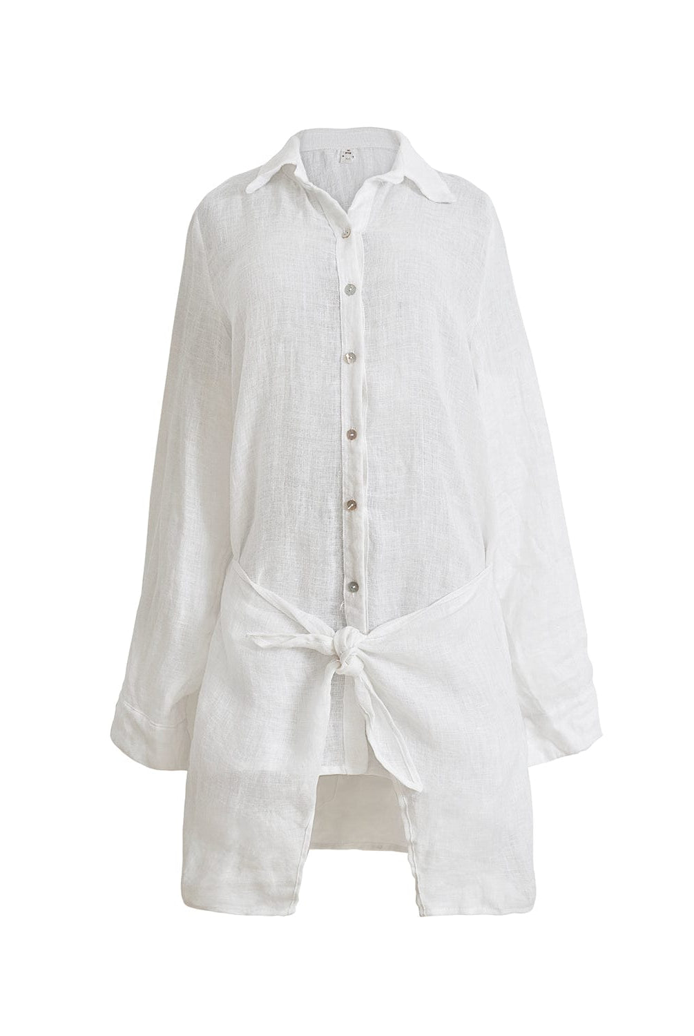 A lightweight white linen button coverup with front-tie detail. Featured against a white wall background.