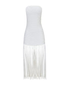 A white strapless fringe hem dress with macramé details. Featured against a white wall background.