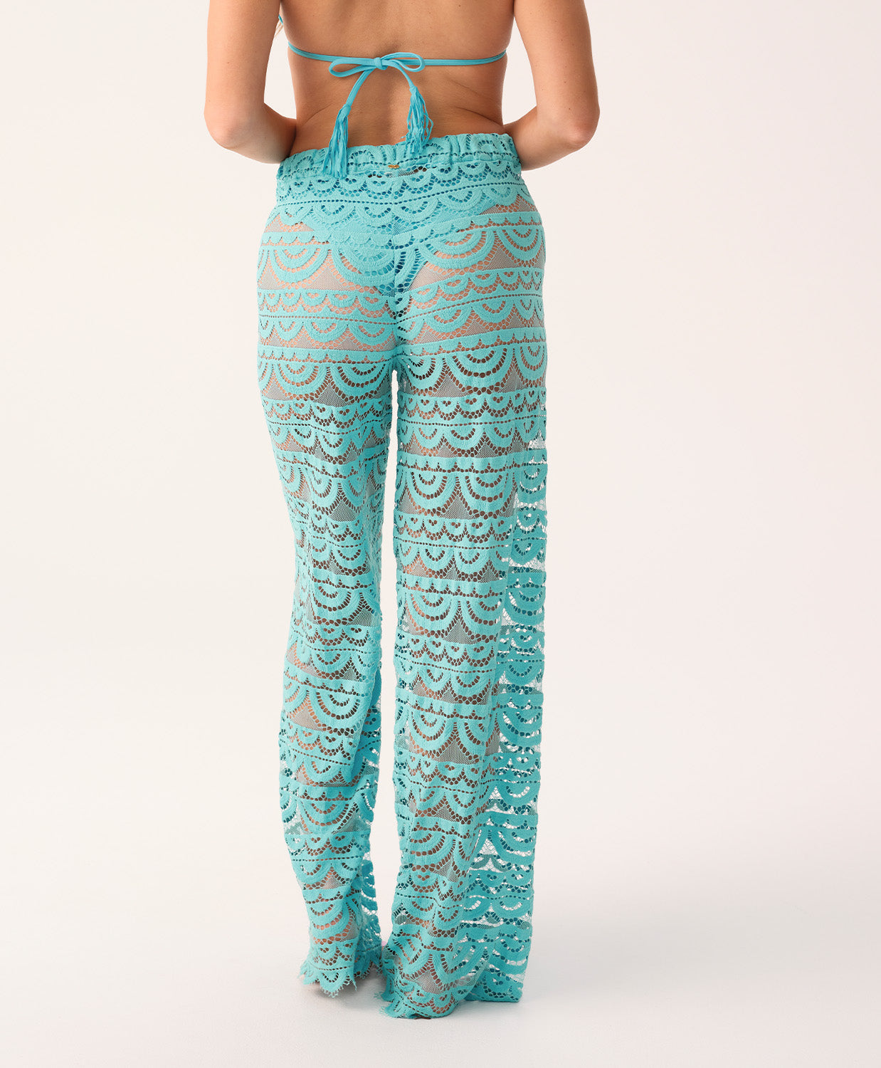 A woman's back, wearing blue high waisted pants and a bikini top on a white background