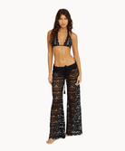 Woman wearing black lace pants and matching top in front of a white background.