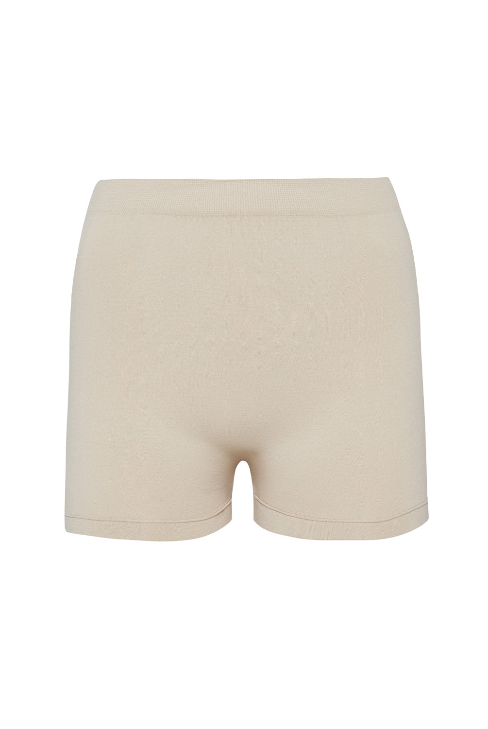 A woman wearing a nude bandeau and matching shorts standing against a white wall.