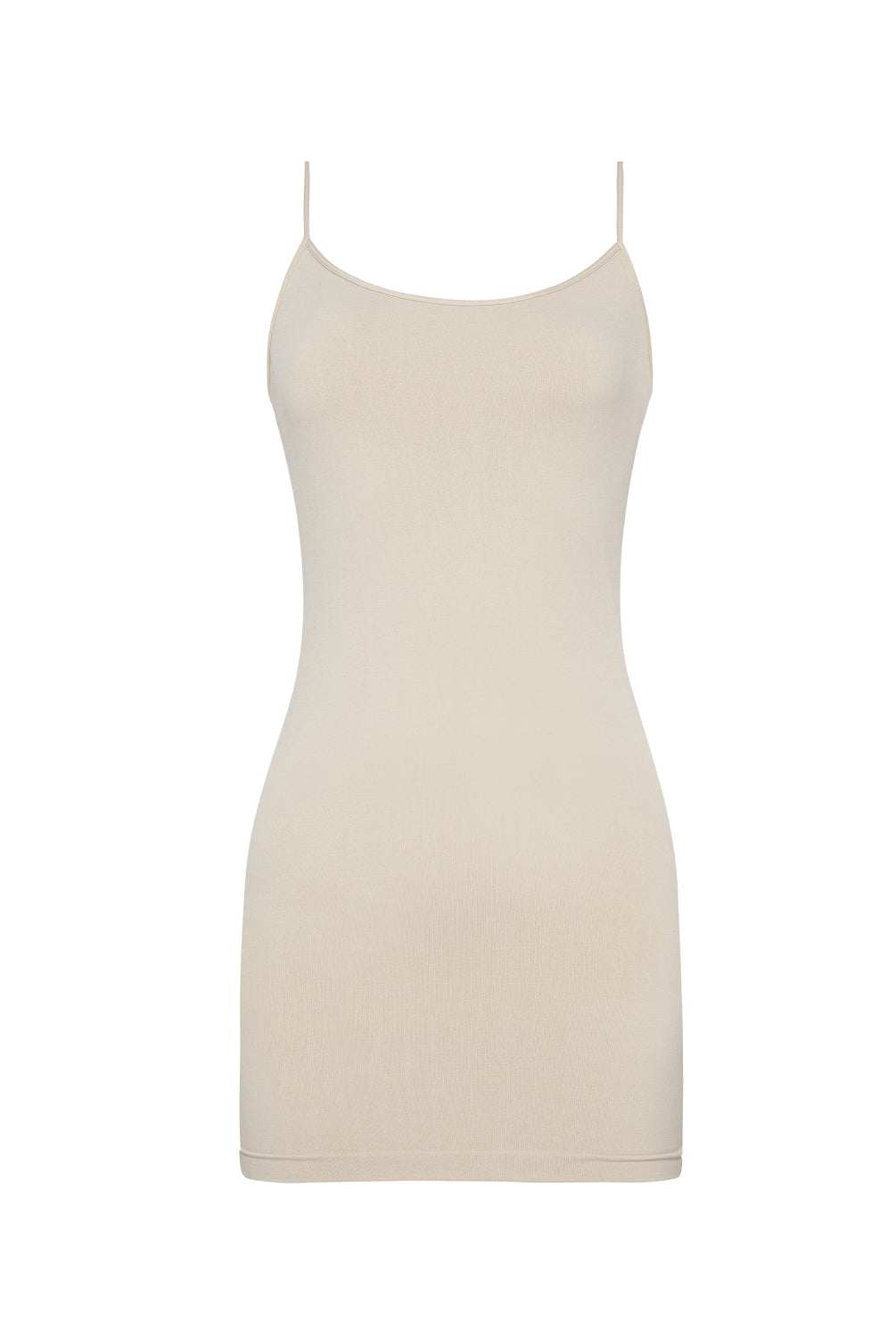 A woman wearing a nude slip dress standing against a white wall.