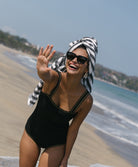 A woman wearing black a one-piece swimsuit with crochet trim details around the neck and shoulders standing on the beach