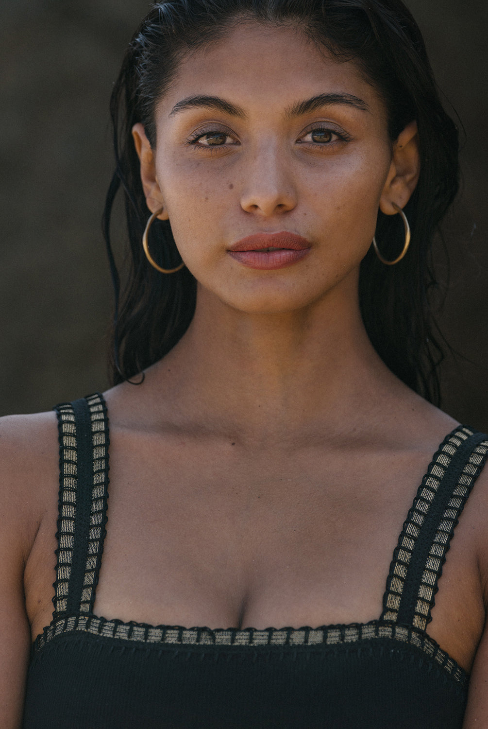 A woman wearing black a one-piece swimsuit with crochet trim details around the neck and shoulders standing on the beach