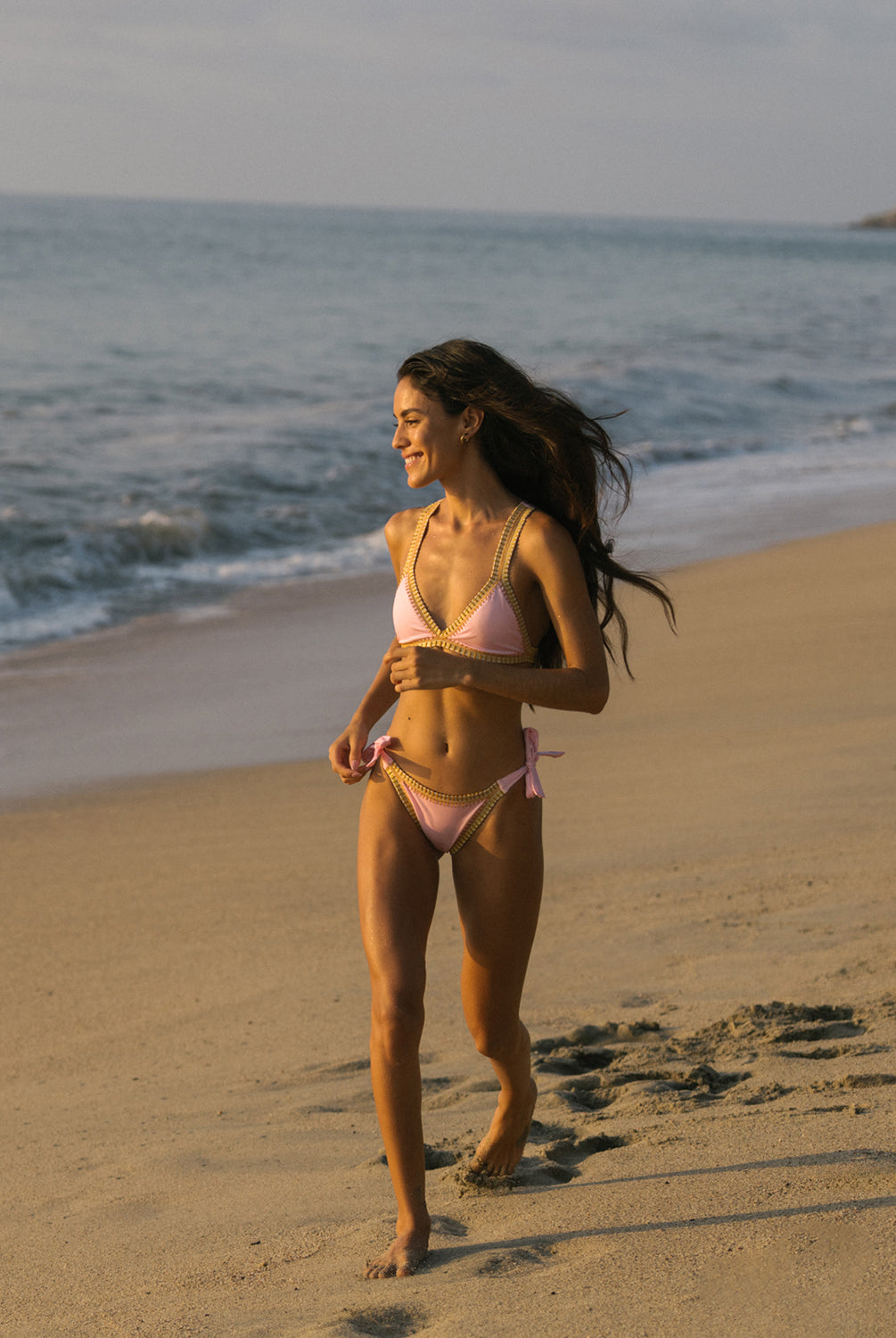 A woman wearing a pink crochet-trim sporty top and matching bottoms with a tropical backdrop.