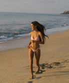 A woman wearing a pink crochet-trim sporty top and matching bottoms with a tropical backdrop.