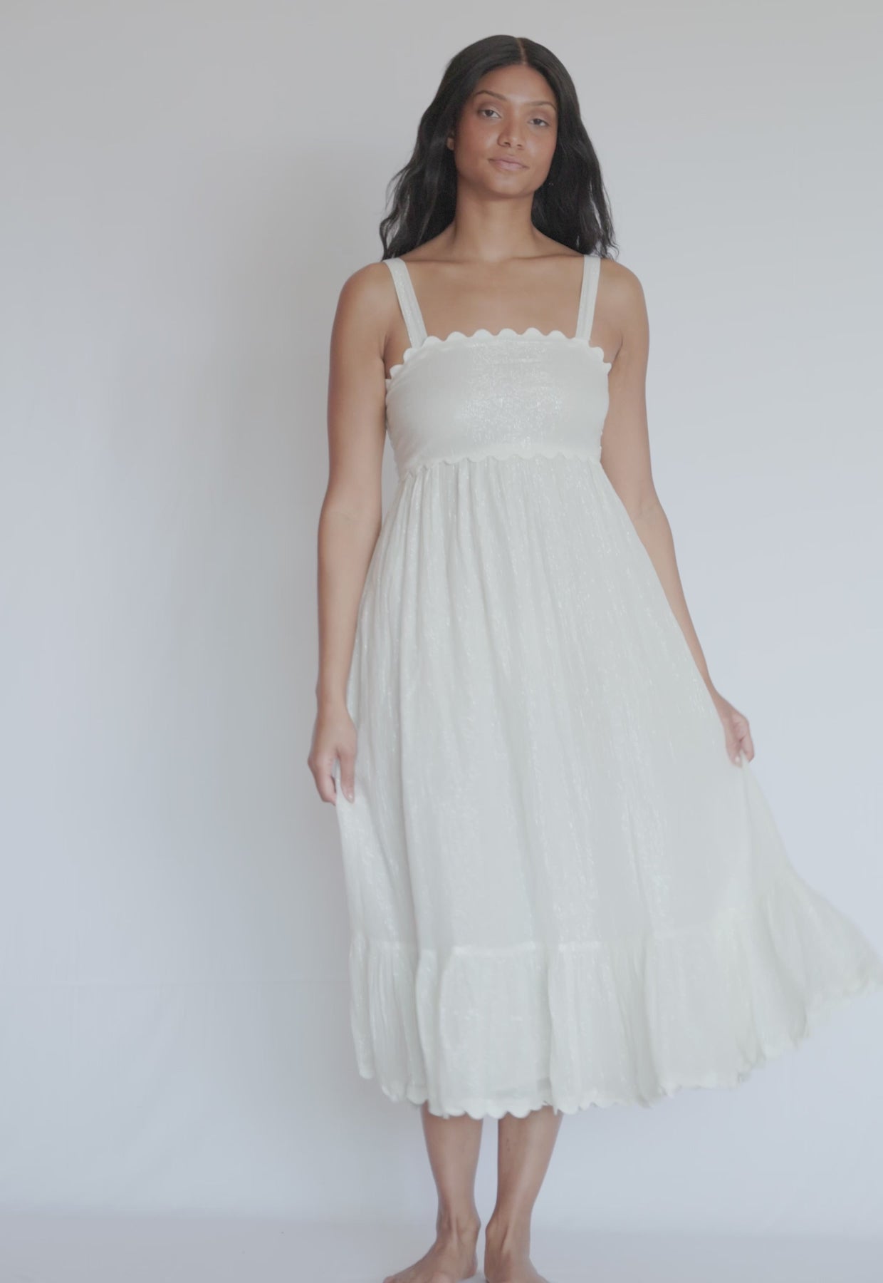 A woman wearing a white mid length dress spinning in front of a white wall.