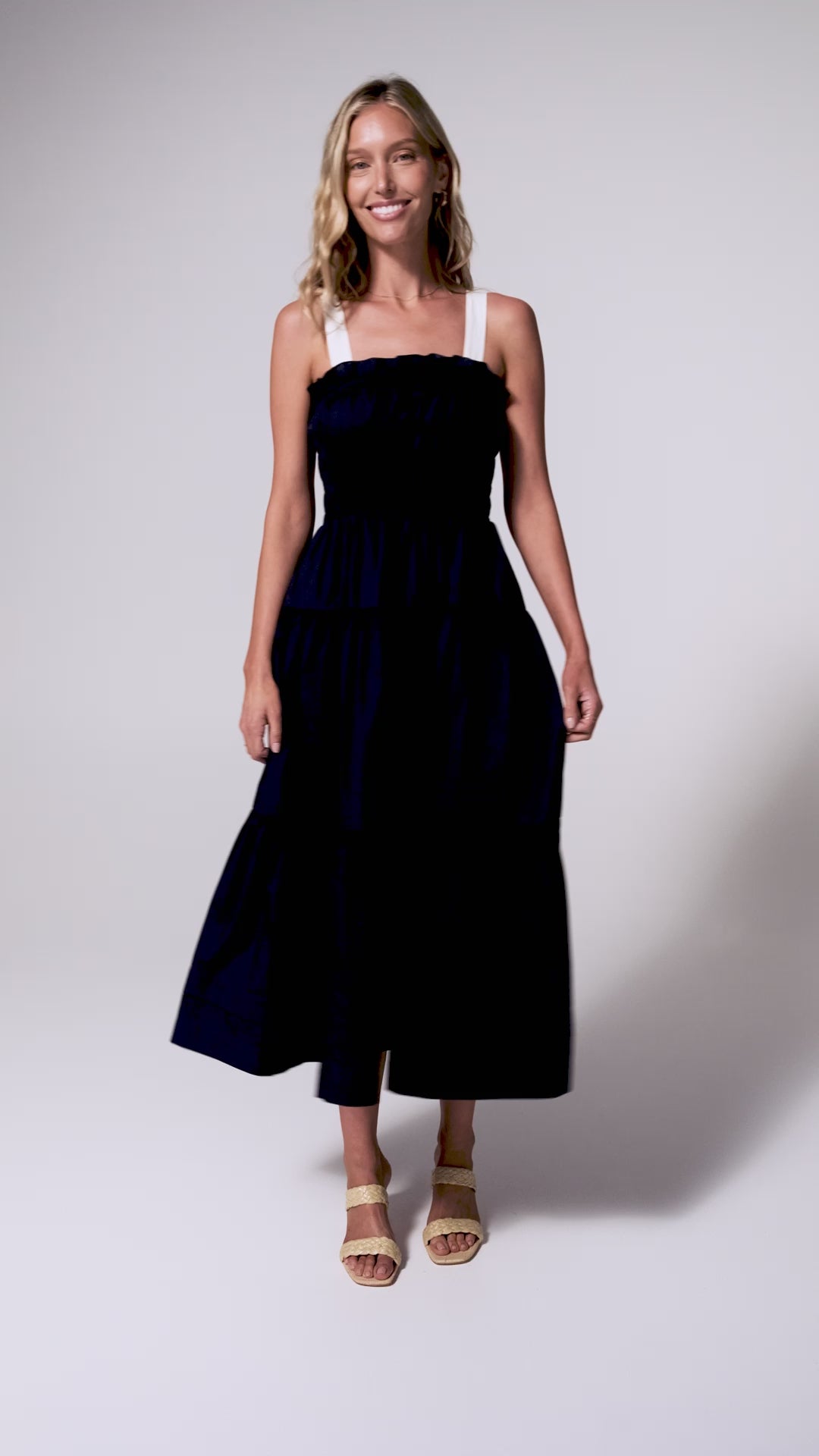 A woman wearing a navy dress with white straps spinning against a white wall.