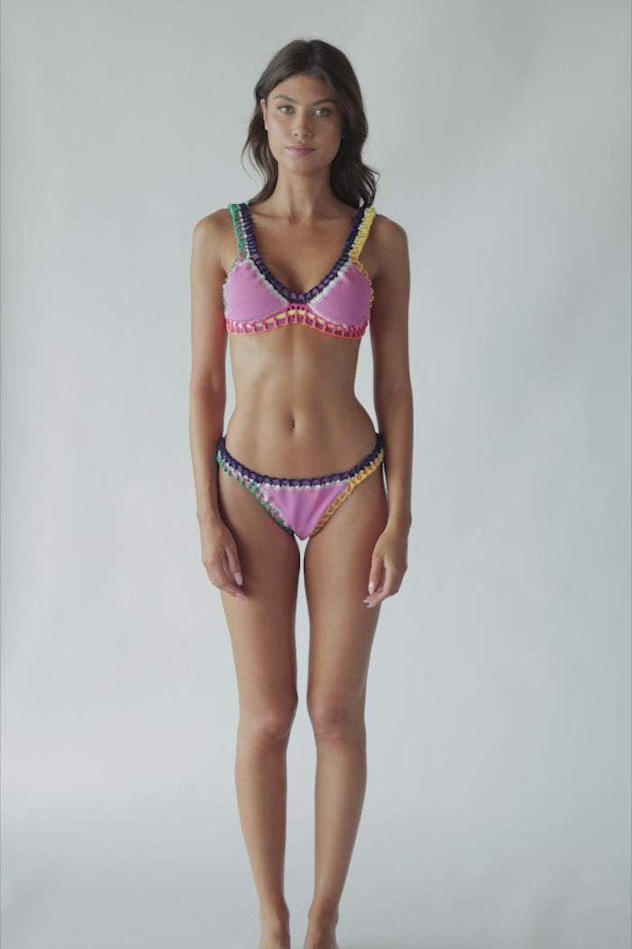 A brunette woman wearing a pink bikini spinning in front of a white wall.