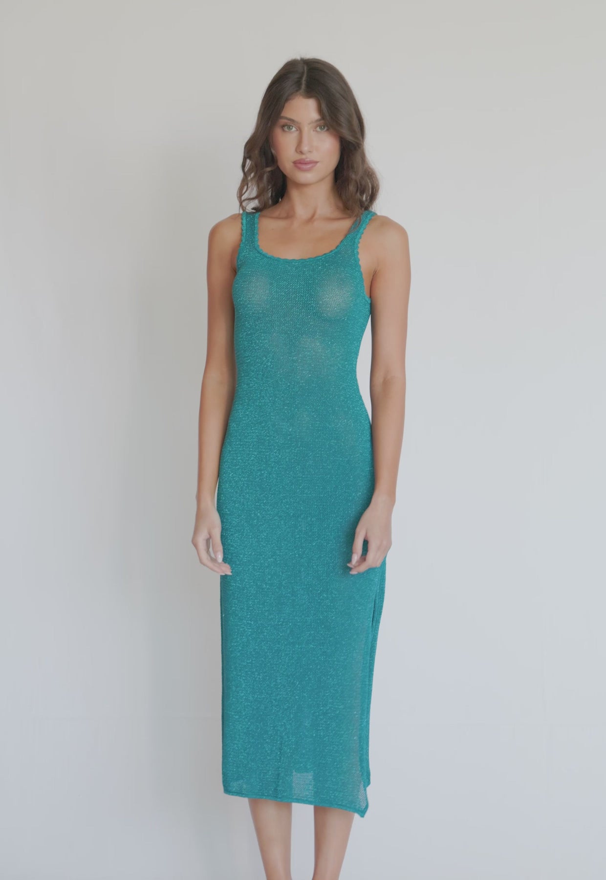 A woman wearing a teal mid-length dress spinning in front of a white wall.
