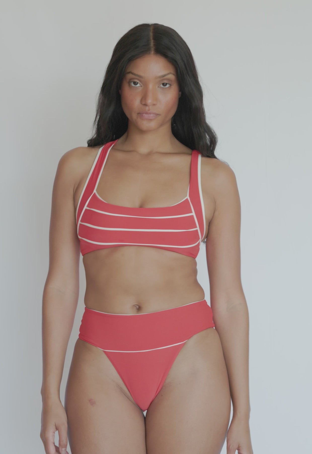 A woman wearing a high waist red bikini spinning in front of a white wall.