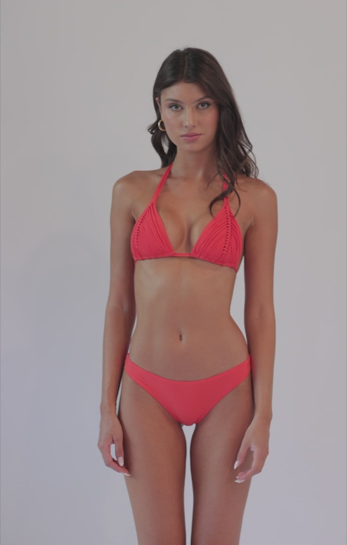 Brunette woman wearing a red macrame bikini spinning in front of a white background.