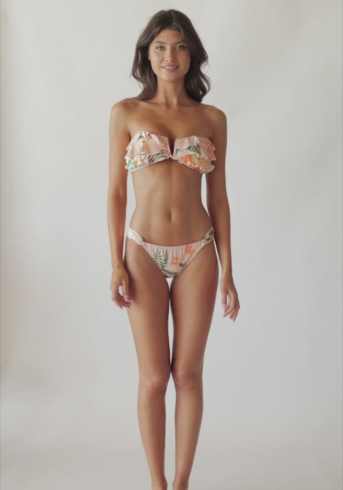A brunette woman wearing a bikini with a tropical print spinning in front of a white wall.