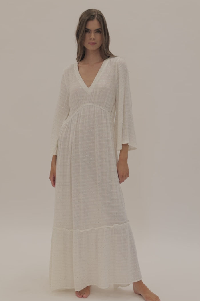 A woman wearing a long sleeve white dress spinning in front of a white wall.