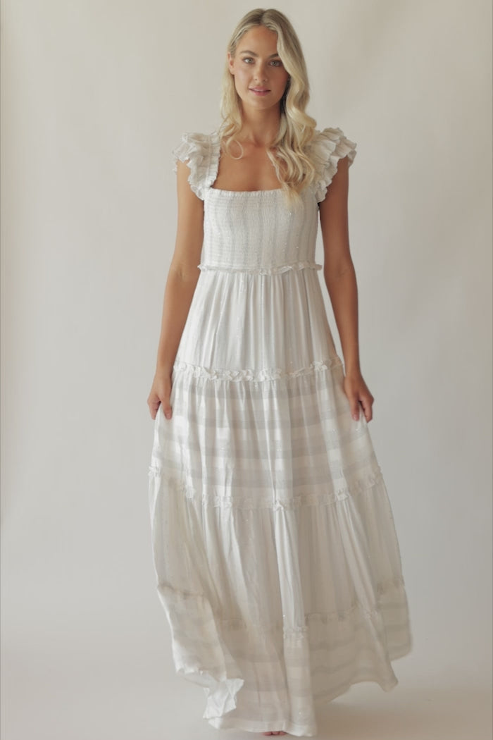 A blonde woman wearing a long white dress spinning in front of a white wall.