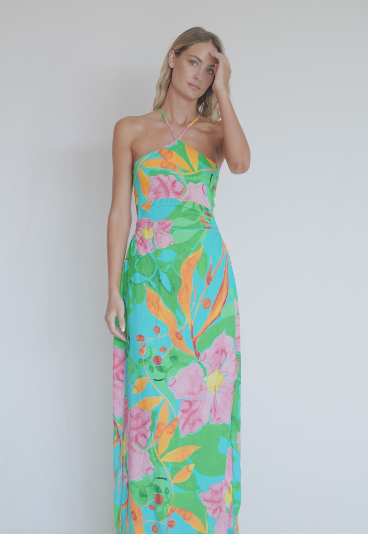 A woman wearing a long floral print dress spinning in front of a white wall.
