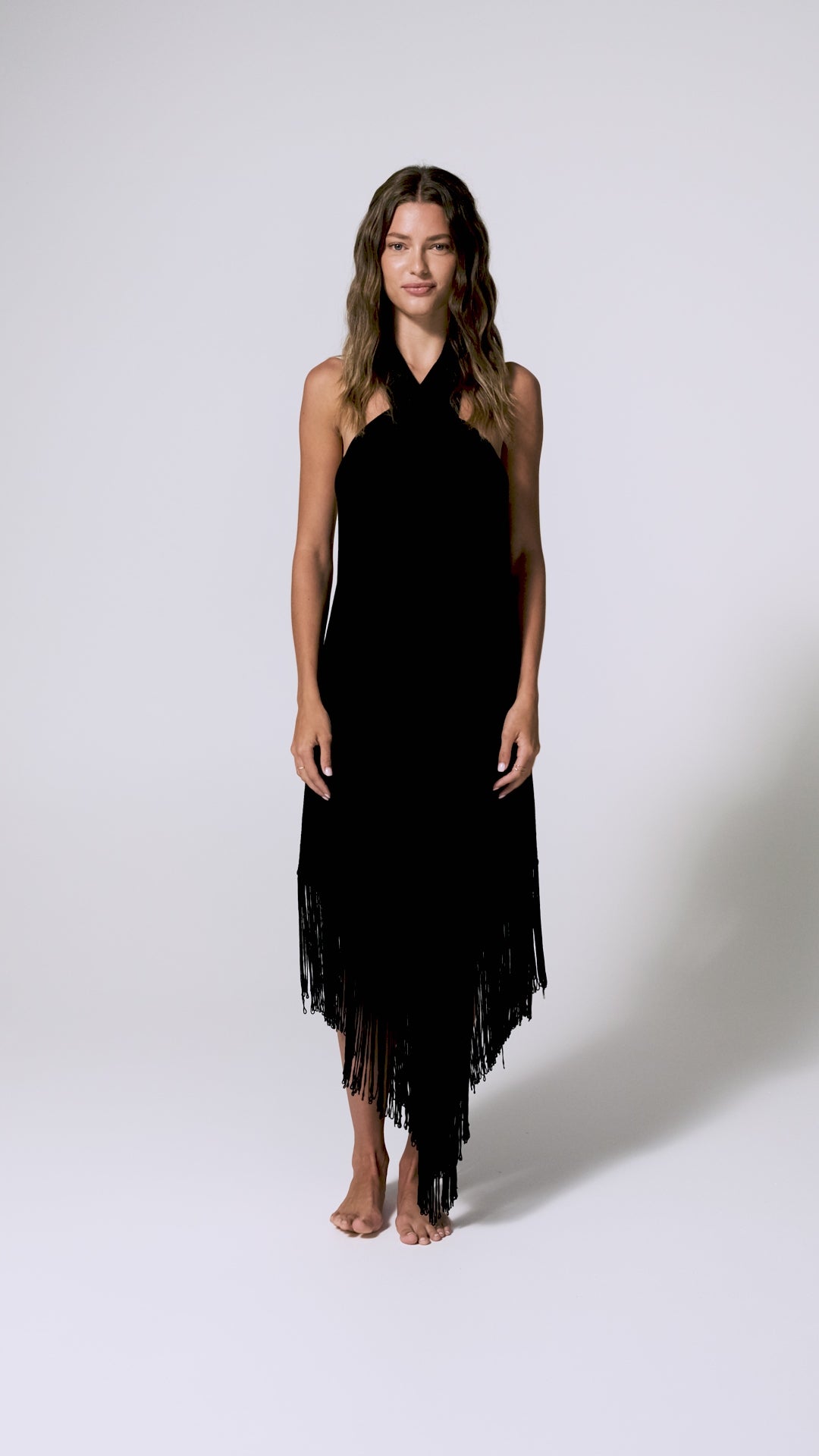 A woman wearing a black tie around the neck dress spinning in front of a white wall.