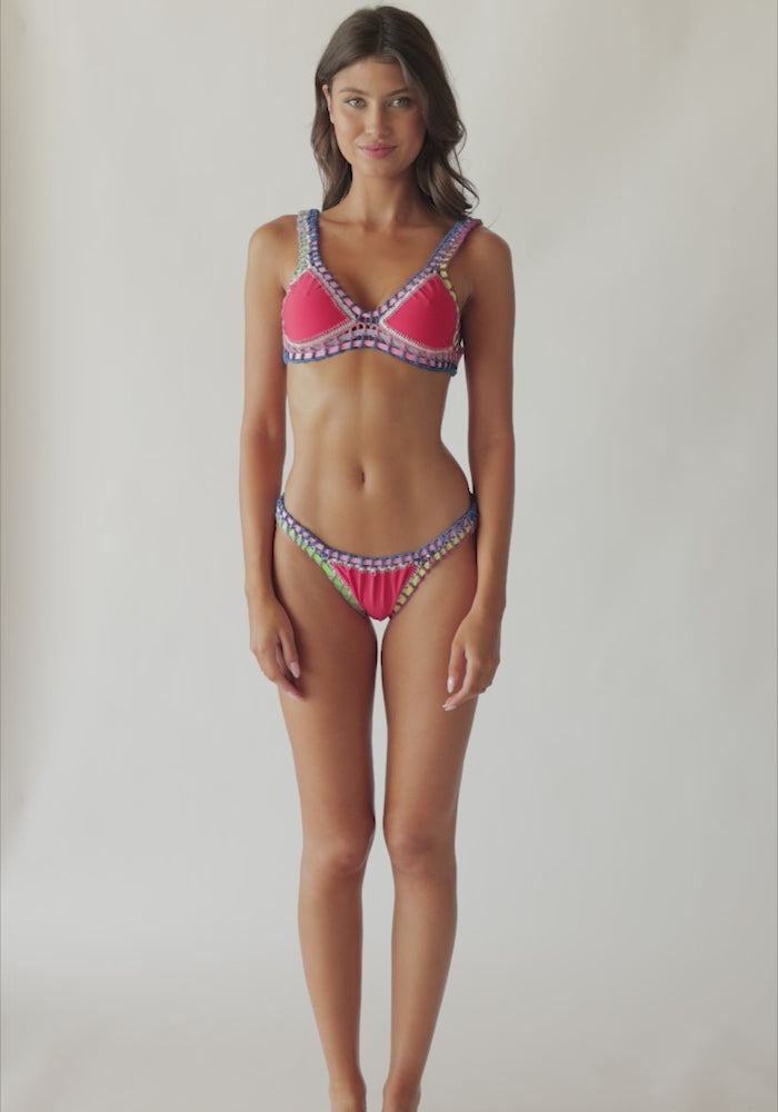 A brunette woman wearing a red bikini spinning in front of a white wall.