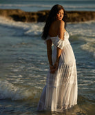 A woman wearing a white long dress standing on a beach in the ocean.