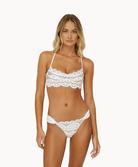 Woman wearing white laced bikini in front of a white background.