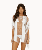 Woman wearing a white fringe cover up in front of a white background.