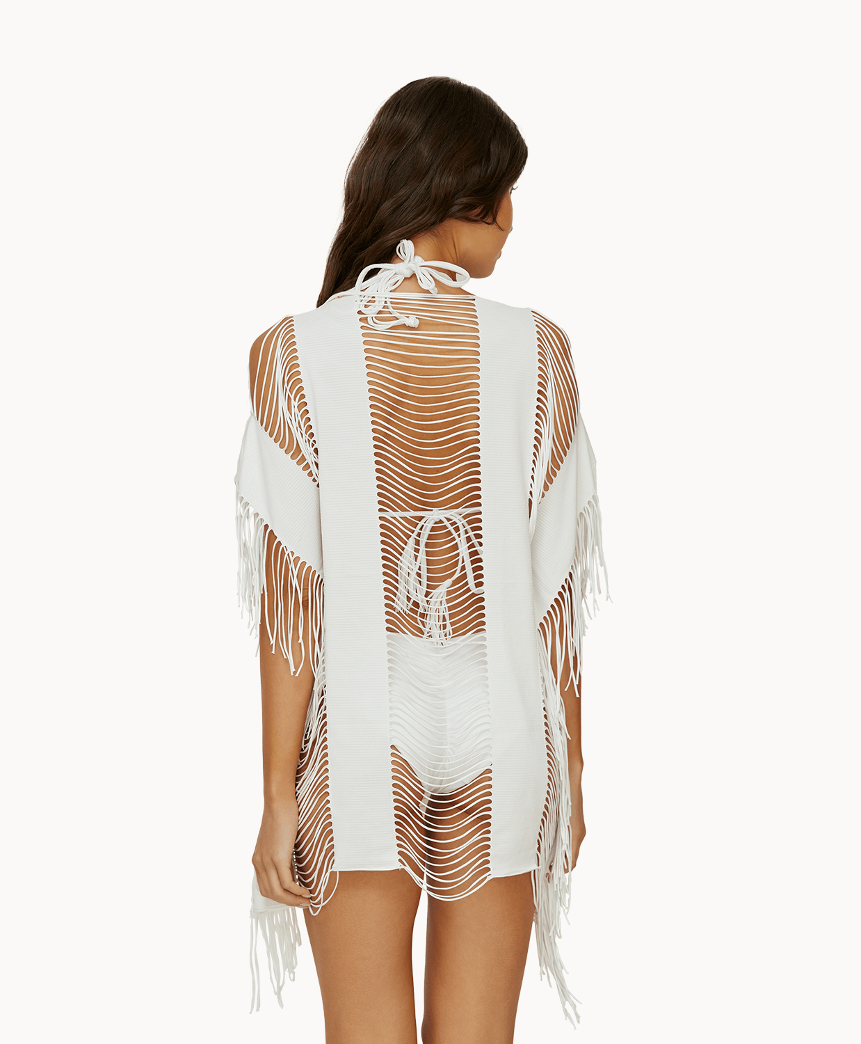 Back view of woman wearing a white fringe cover up in front of a white background.