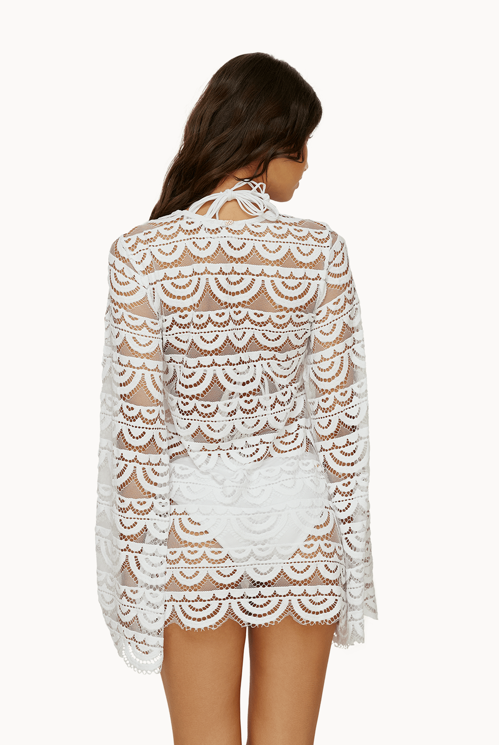 Back view of woman wearing a white lace tunic in front of a white background.