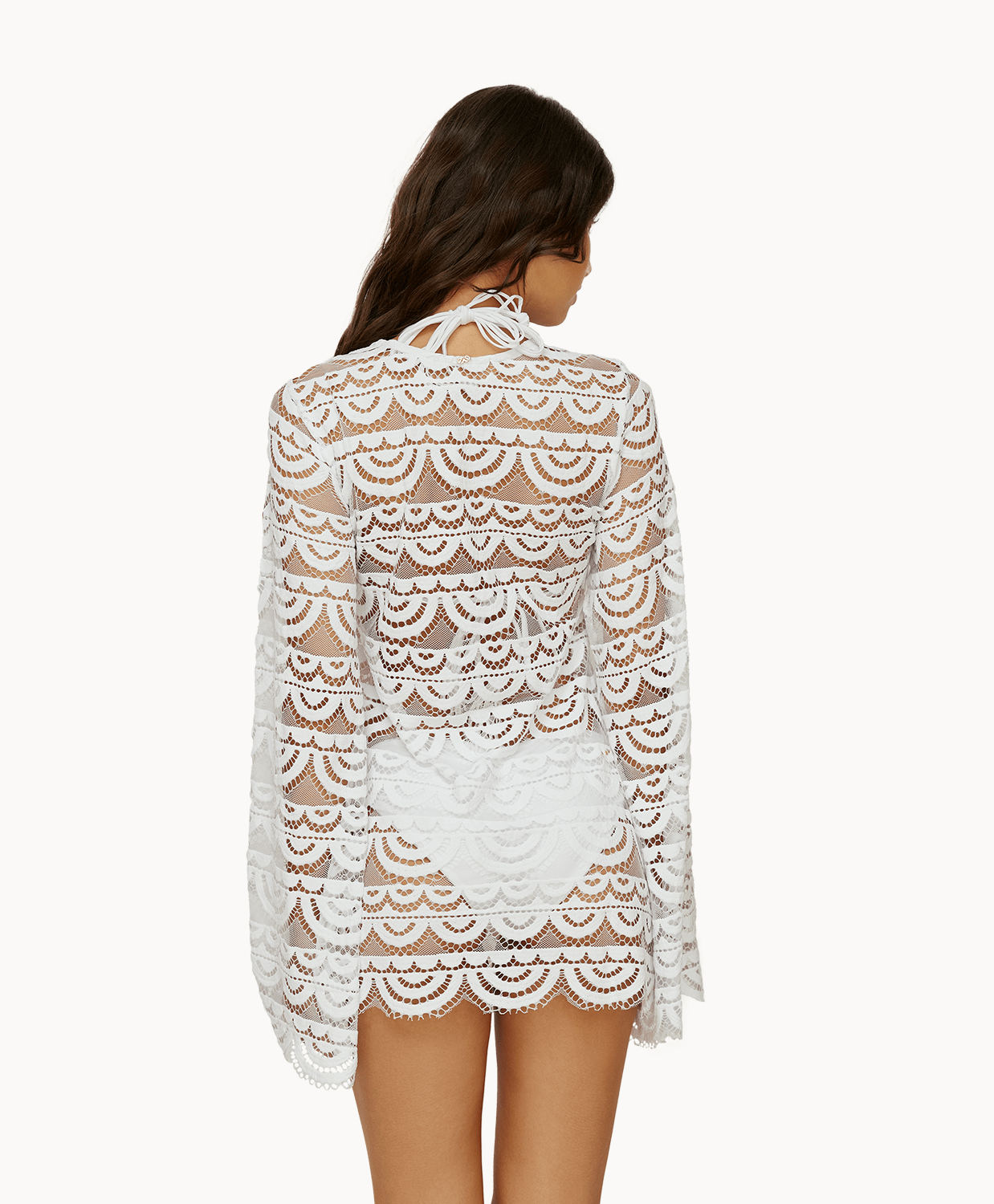 Back view of woman wearing a white lace tunic in front of a white background.