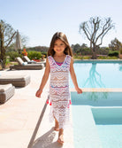 A brunette girl wearing a white lace cover up dress standing near a pool.