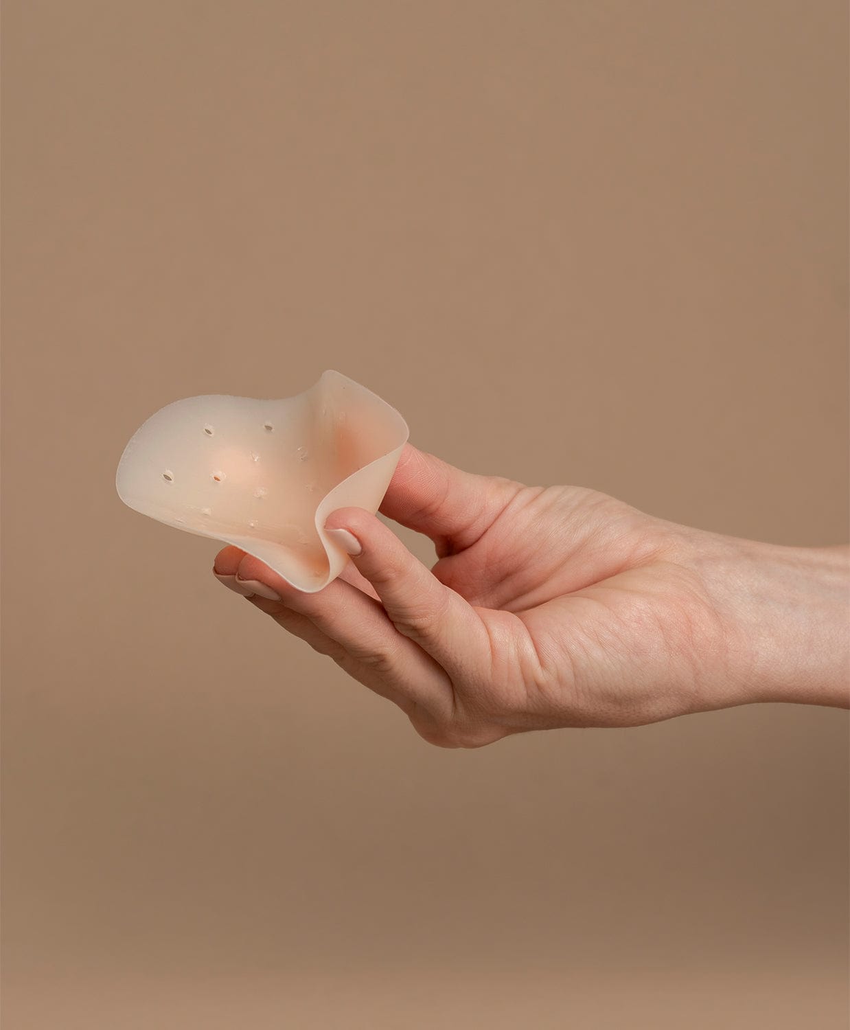 Hand picking up a nipple cover in front of the brown background.