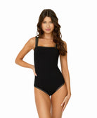 Woman wearing a black one piece in front of a white background.