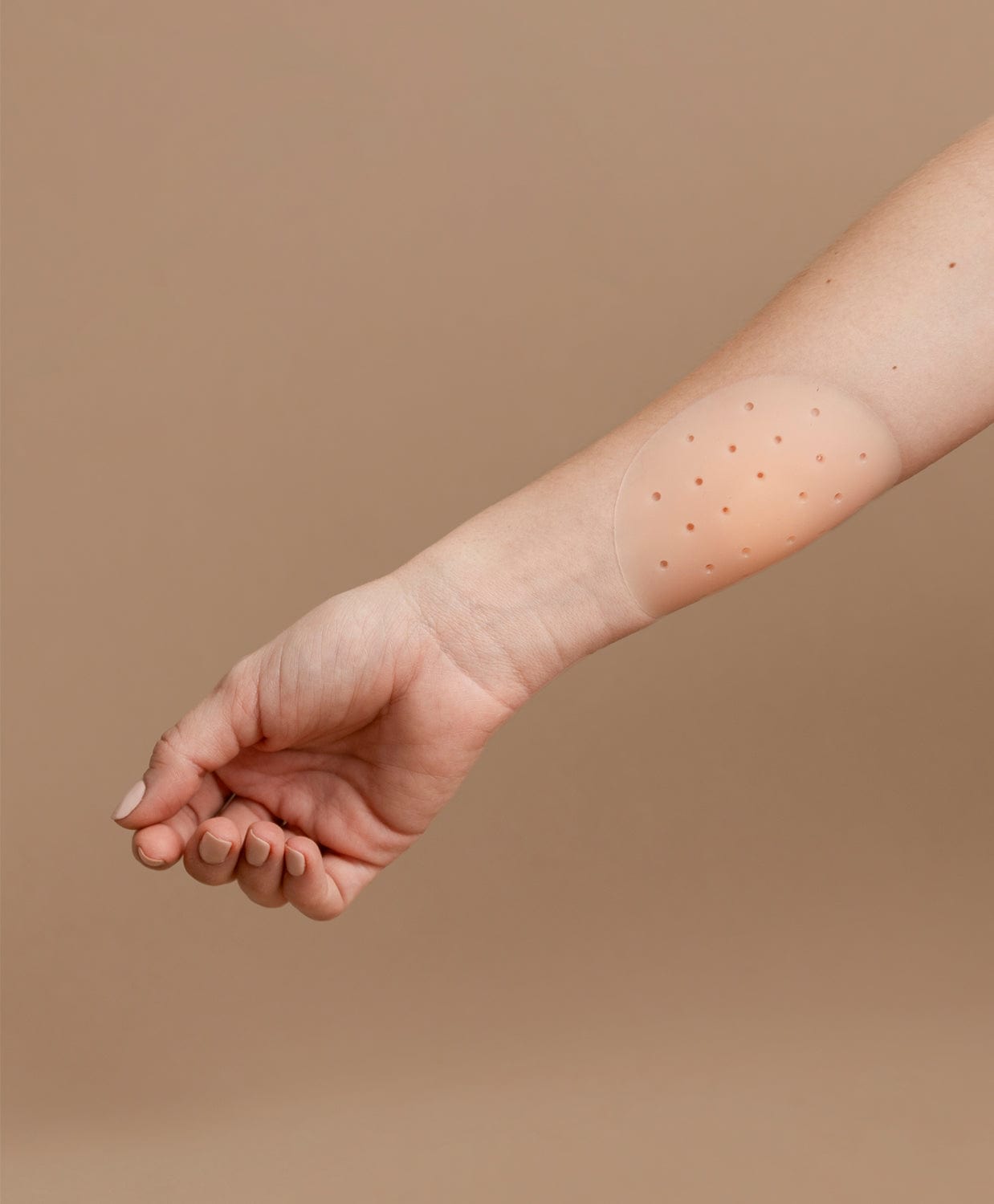 Nipple cover stuck on an arm in front of a brown background.