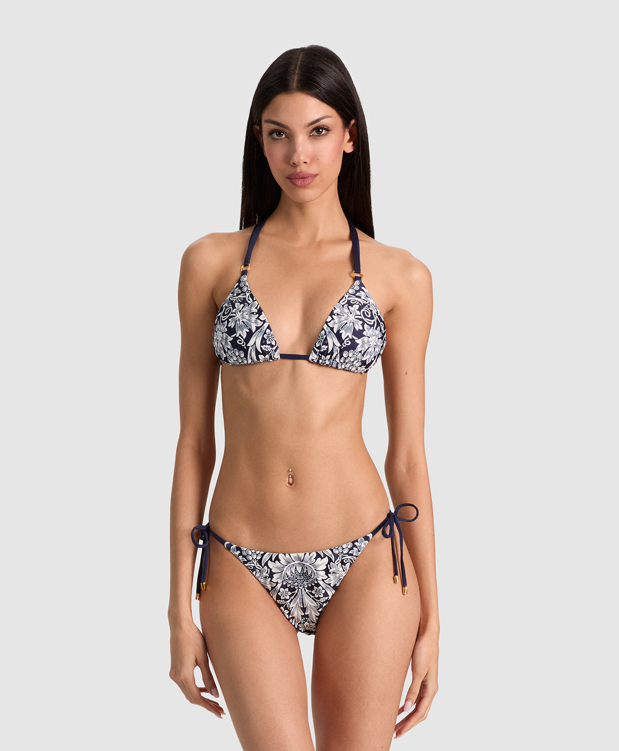 A woman modeling a two-piece string bikini with a navy blue and white floral pattern against a solid light gray background.